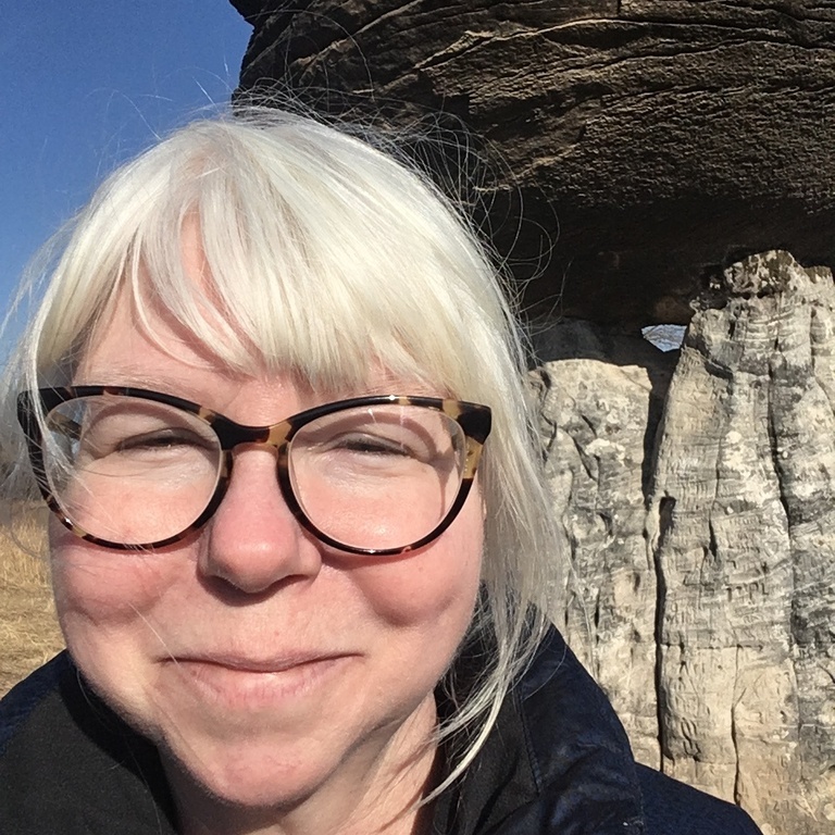Margaret Beck standing in front of Mushroom rock. Margaret has white hair and glasses.